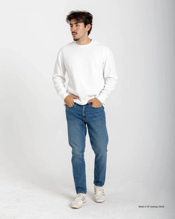 Man wearing a beige checkered shirt and dark jeans on a white background