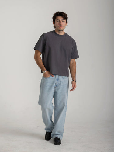 Man wearing a gray t-shirt and light blue jeans on a plain background