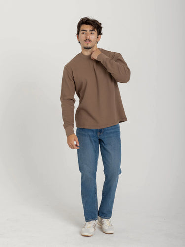 Man wearing a brown sweater and blue jeans on a white background