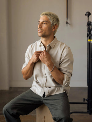 Man sitting on a stool adjusting his shirt in a neutral setting