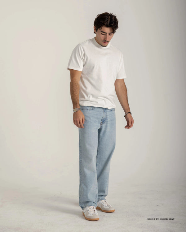Man wearing a white t-shirt and light blue jeans on a plain background