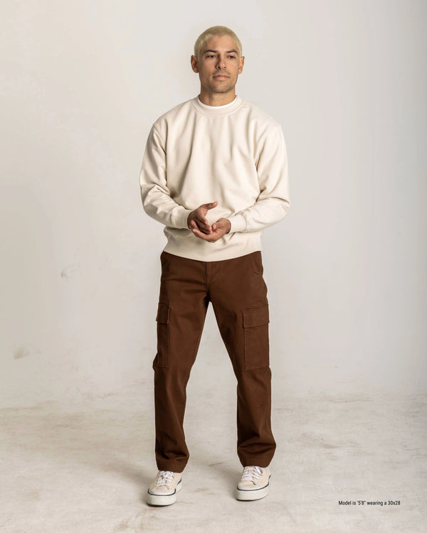 Man wearing a white sweater and brown pants against a plain background