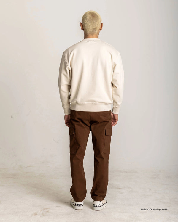 Person wearing a beige sweater and brown pants on a white background