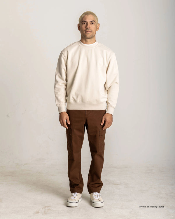 Man wearing a beige sweater and brown pants on a white background
